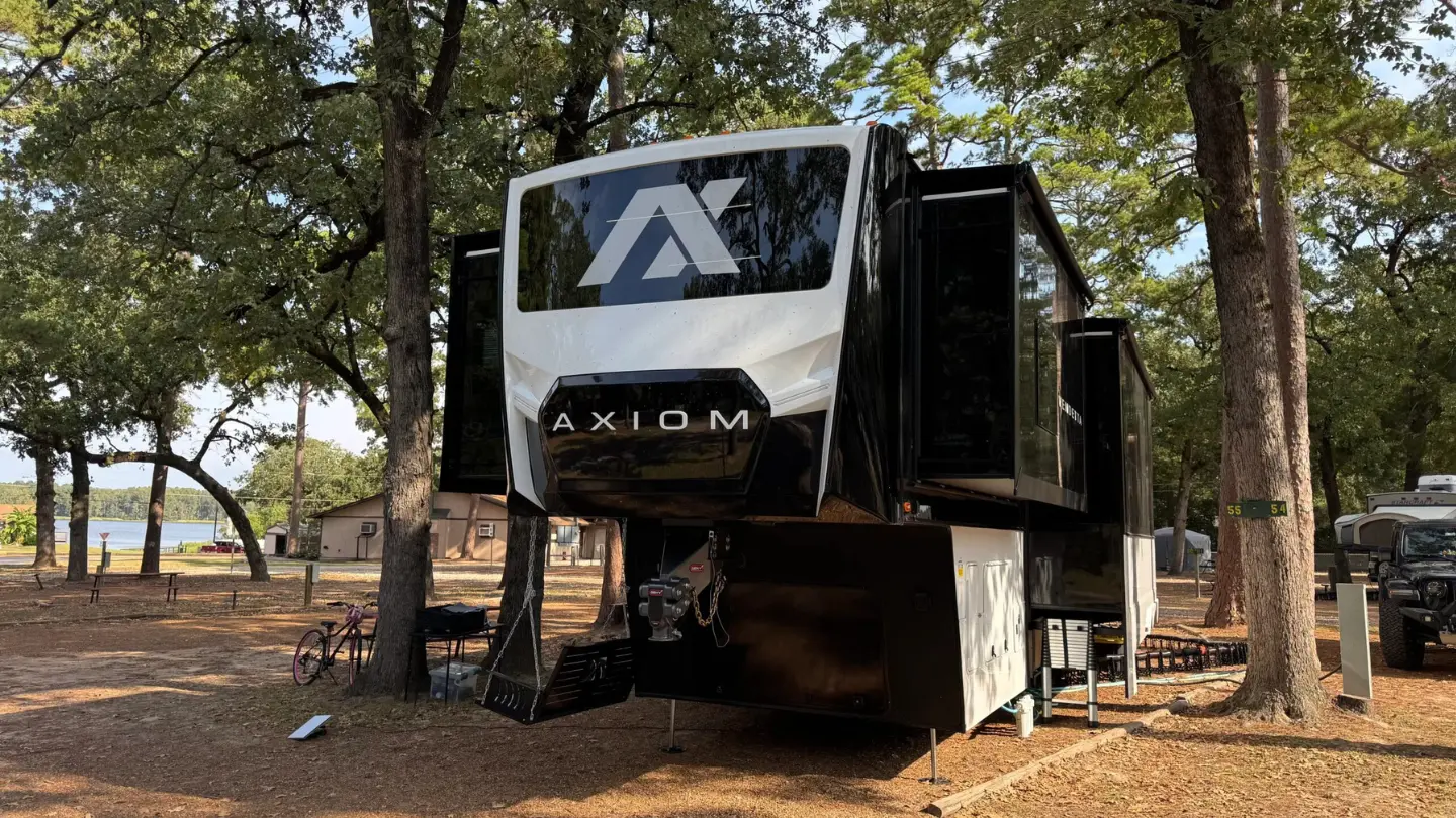 The Lawings Axiom fifth wheel RV parked among tall oak trees beside a lake. the Lawings run a full-time RV family Blog